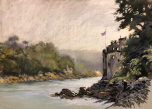 Castle on a riverbank with a flag flying above and misty forested hills in the background.